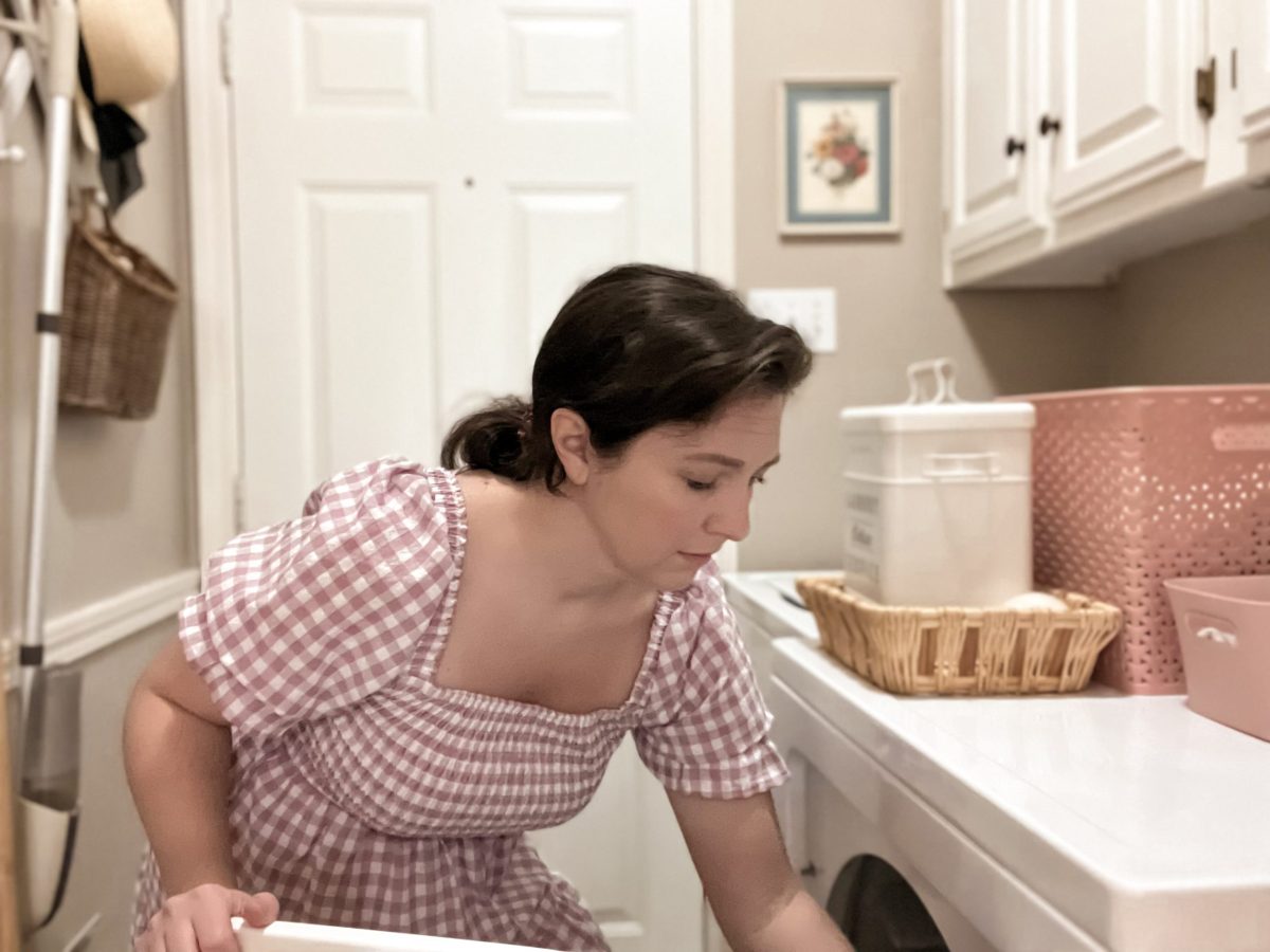 woman in pink gingham dress putting clothes in dryer