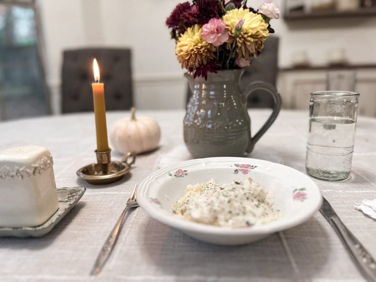 plate of food with a vase of flowers next to a lighted candle