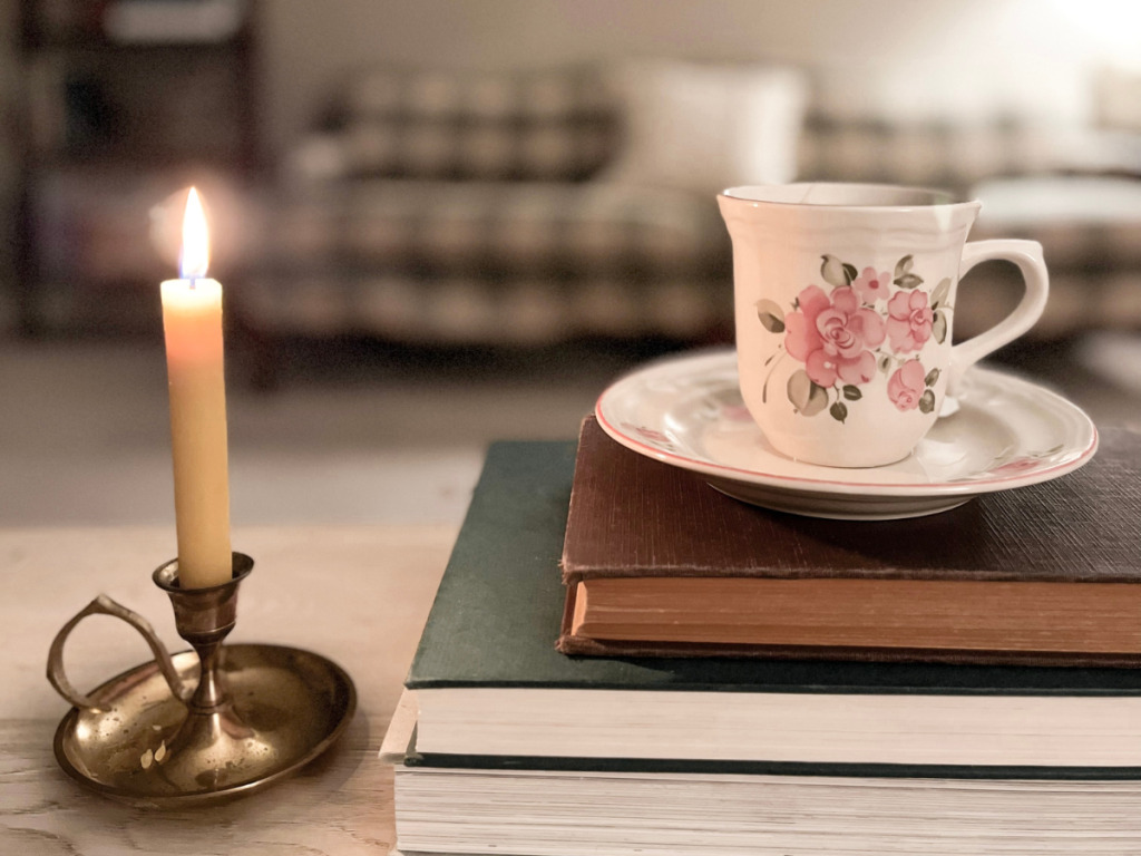 Candlestick lit, floral tea cup on top of stack of old books