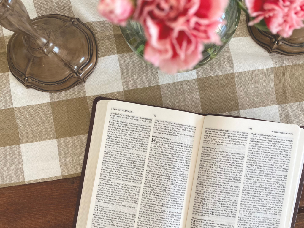 Open Bible on gingham table runner, flowers peeking overhead, candle stick holder