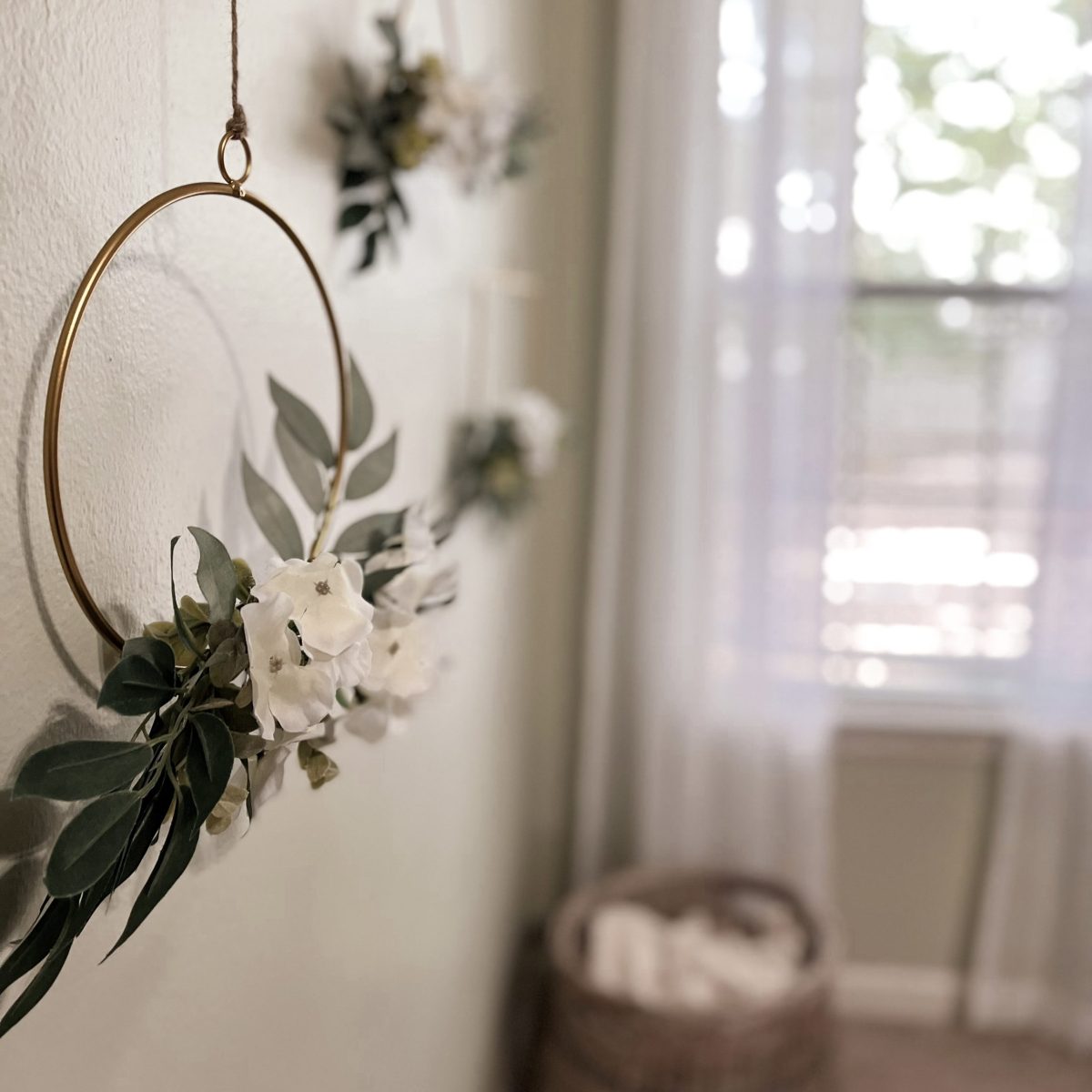 Floral gold wreath hanging on sage green wall, white curtains on window in background
